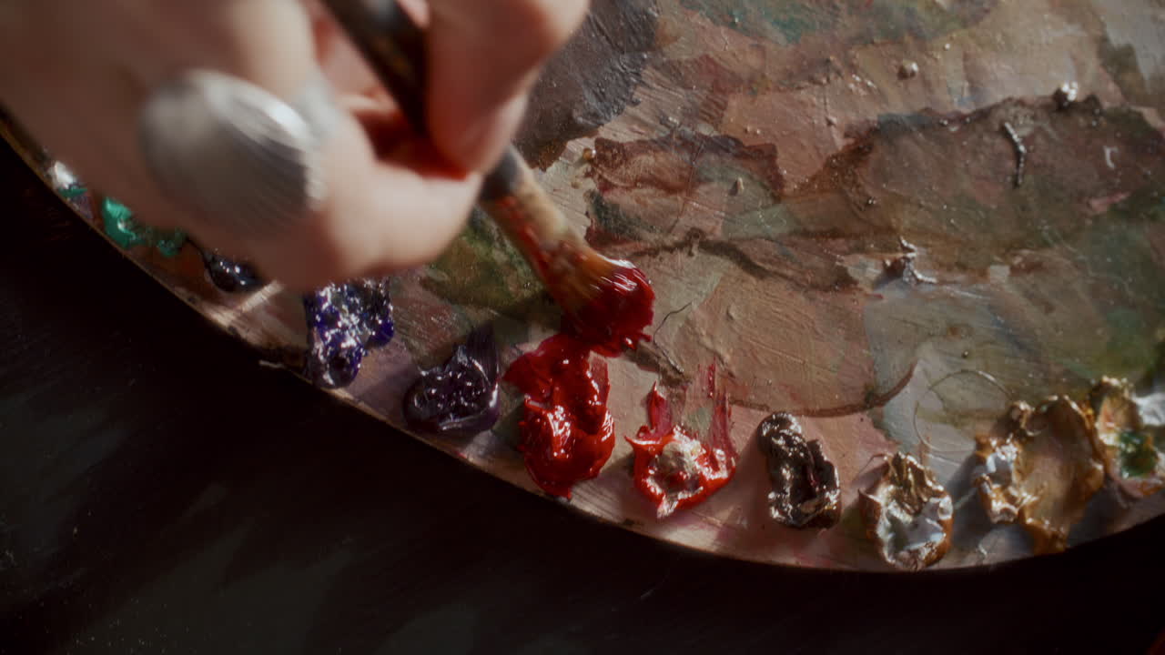 Hand des Künstlers, der rote Ölfarbe auf einer Palette mit einem Pinsel mischt