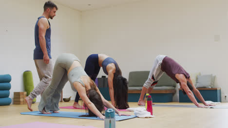 Vielfältige-Gruppe-übt-Yoga-Pose-Im-Unterricht-Mit-Männlichem-Lehrer,-Der-Hilft