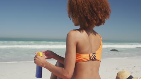 mujer afroamericana aplicando protector solar en la playa