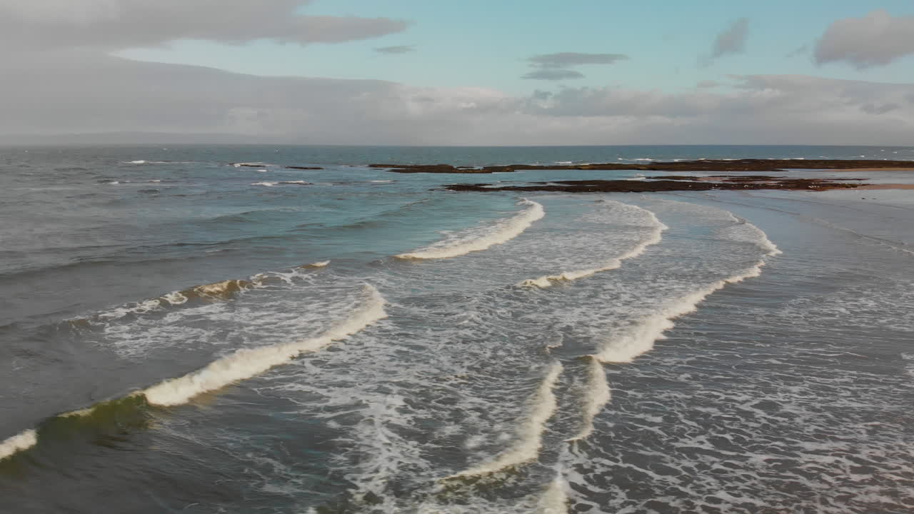 pequeñas olas rodando en la playa escocesa con nubes en el cielo arriba