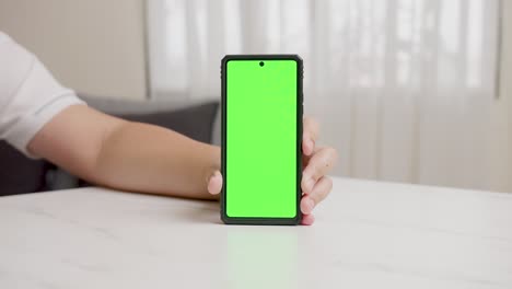 man's hand shows mobile smartphone with green screen in vertical position isolated on green background