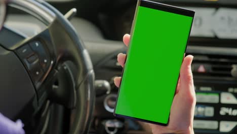 la mano de la mujer del conductor en el coche utiliza un teléfono inteligente con una pantalla verde, dentro de un coche.