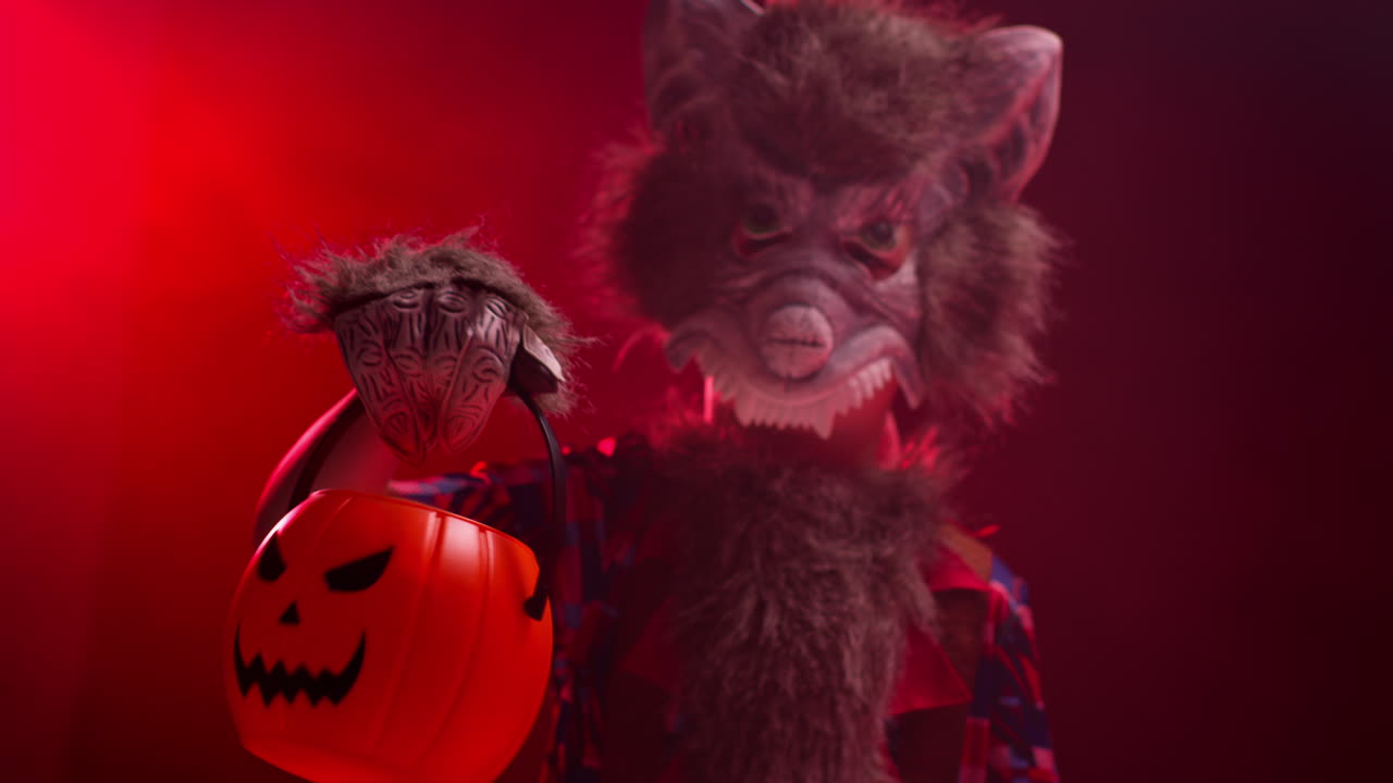 fotografía de estudio de un niño disfrazado de hombre lobo monstruo truco o trato en halloween con humo rojo iluminación de fondo sosteniendo balde en forma de calabaza jack o'lantern 1