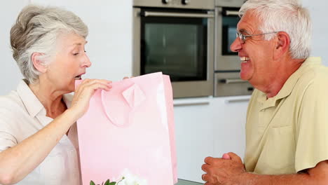 un hombre mayor le da a su compañero un regalo en una bolsa rosa.