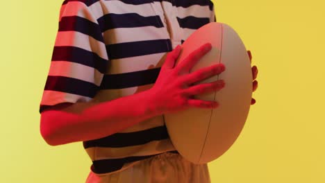 caucasian female rugby player with rugby ball over neon yellow lighting