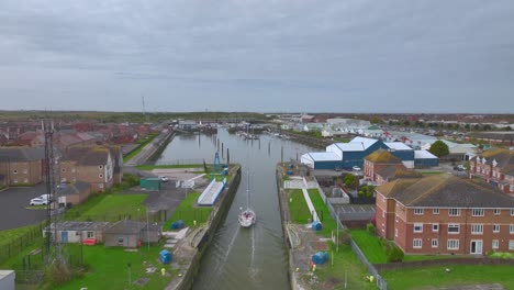 Yacht-heading-through-narrow-canal-entering-marina-on-calm-water