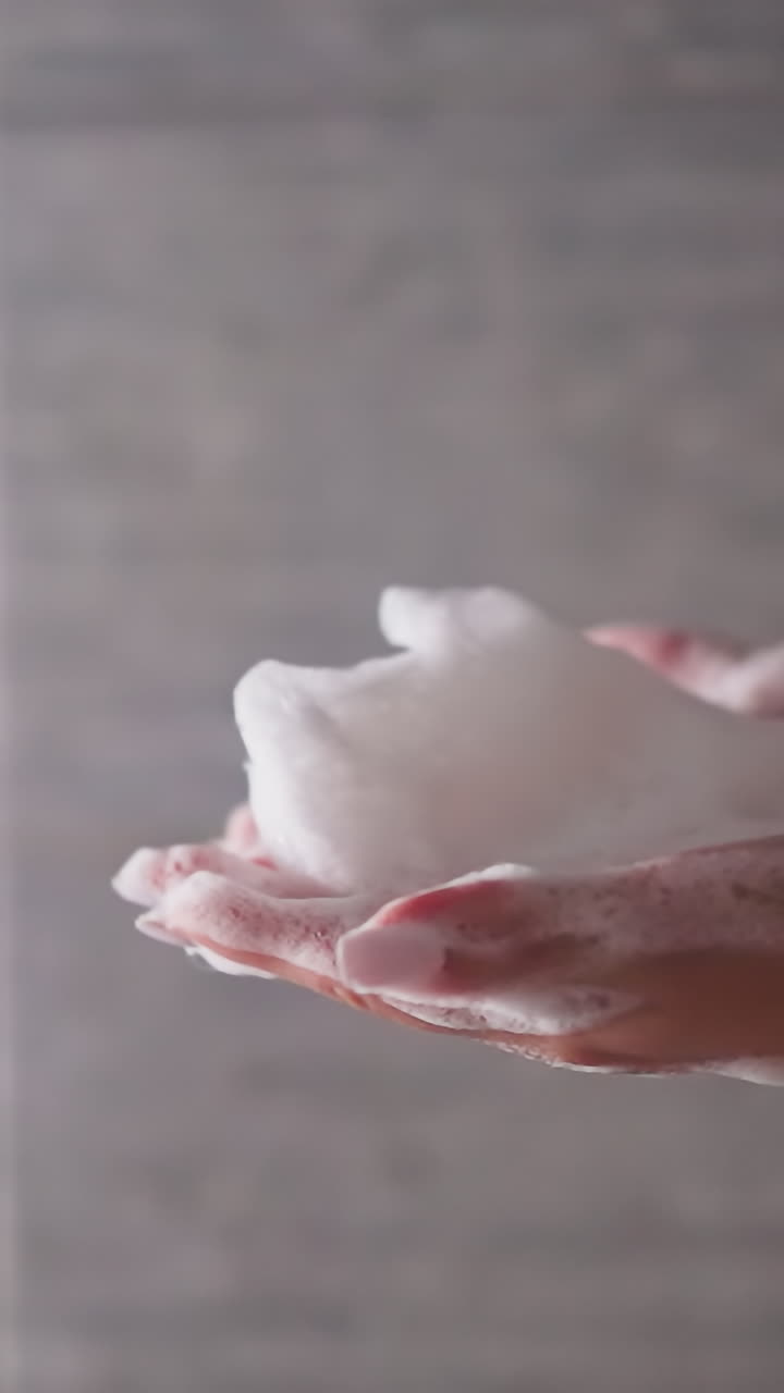 las manos de la mujer sostienen la espuma soplada de las palmas en el primer plano de la cabina de ducha. la dama juega con espuma esponjosa mientras se baña en el baño de la casa. producto cosmético higiénico