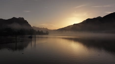 the peaceful and serene atmosphere over walensee lake in switzerland, with the sun fading behind hills and a misty and foggy water surface, creates a tranquil and dreamy scene.