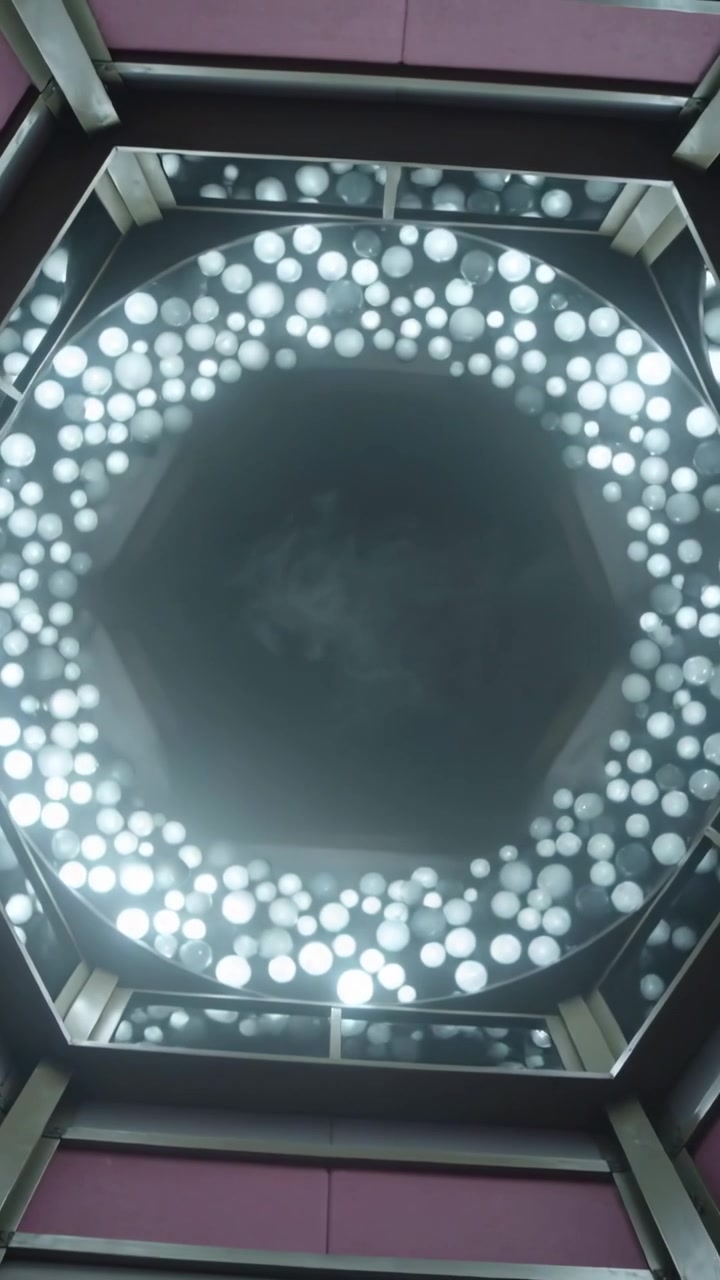 Video verticale: Telefono inclinato che rivela un apparecchio rotondo nella hall, con un anello LED esagonale centrale pulsante.