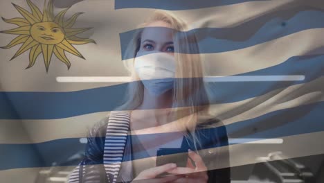 Animation-of-flag-of-uruguay-waving-over-caucasian-woman-wearing-face-mask-in-city-street