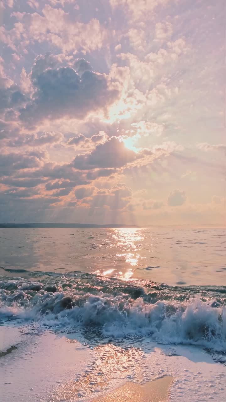Low-angle video shot of a serene beach at sunset, capturing gentle waves and a dramatic sky with sun