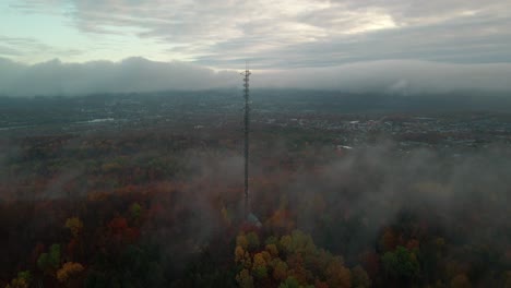 flying towards the communication tower surrounded by the autumnal trees on a foggy morning in quebec, canada