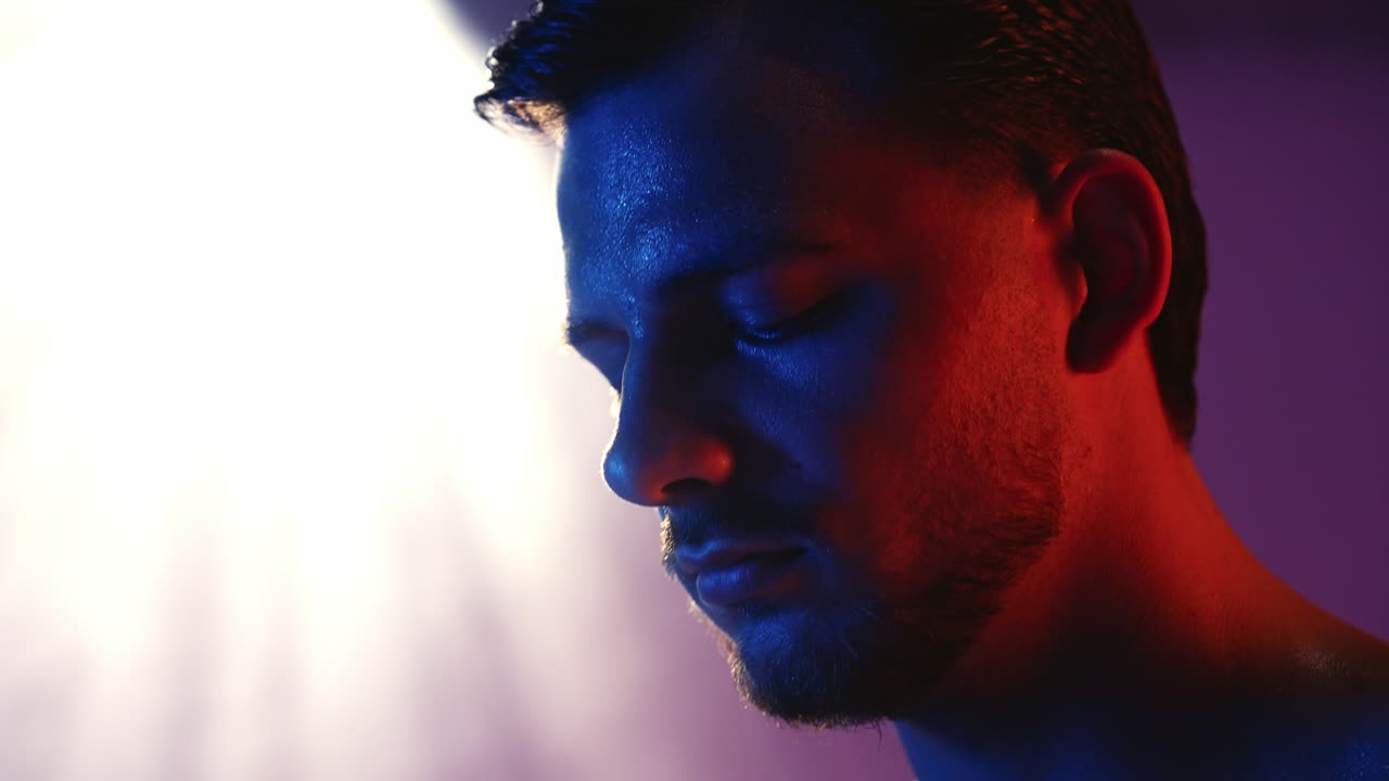 Intense close-up of a male boxer’s face as he looks down, focused while putting on gloves, lit by dramatic orange and blue cinematic lighting