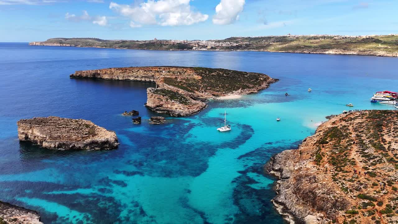 Den Blå Lagune i Comino, Għajnsielem, Gozo-regionen, Malta, med lavt turkist bassin over karbonatbund og kalkstensøer mellem Comino og Cominotto, klart middelhavsvand, langsom drone-tilbagetrækning