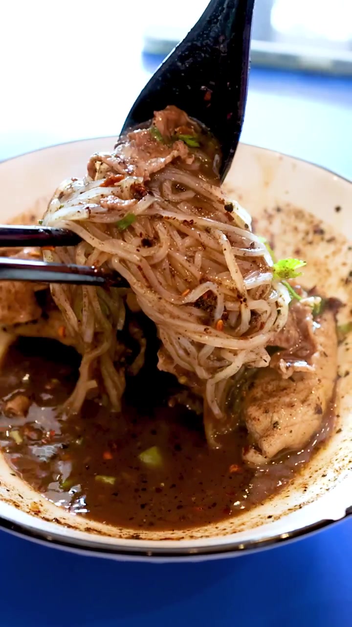 Una persona usa bacchette e un cucchiaio per sollevare noodles di manzo piccanti da una ciotola