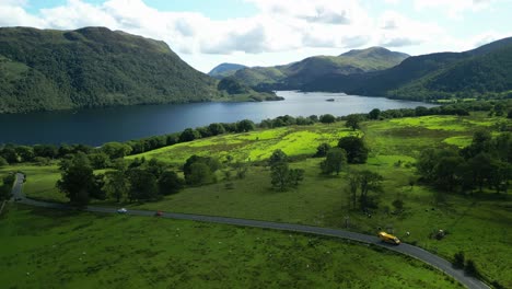 Dark-lake-surrounded-by-wooded-mountains-on-bright-summer-day-with-road-A5091-bending-towards-lake-with-traffic