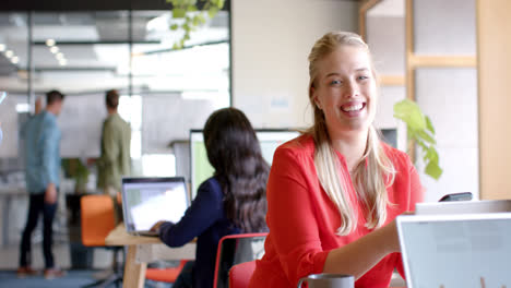 retrato de una feliz mujer de negocios caucásica usando un teléfono inteligente en una oficina casual, en cámara lenta