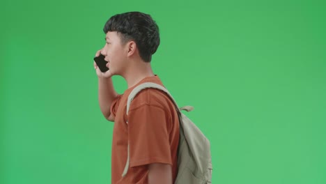 The Side View Of Asian Boy Student Talking On Mobile Phone While Walking To School On Green Screen Chroma Key