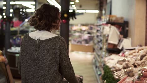 rare view of a woman is driving shopping trolley through food department in supermarket and looking around, picking bag with