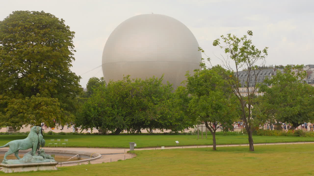 The Olympic cauldron soars in a hot air balloon against the backdrop of Tuileries Gardens, showcasing a stunning display of the torch's flame.