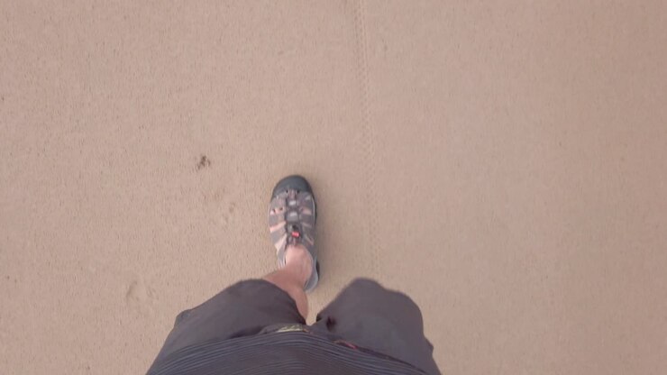 POV di un uomo che cammina indossando una scarpa su una spiaggia di sabbia bianca al rallentatore durante le vacanze estive