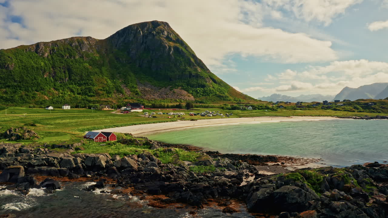 Aerial drone shot of the picturesque green landscape of the Lofoten islands, Norway. Bird's eye view of the white sanded beach, sea mountain in the background.