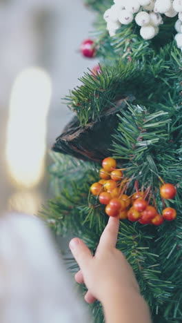 blond little girl touches orange decorative berries on christmas wreath in light room extreme close view