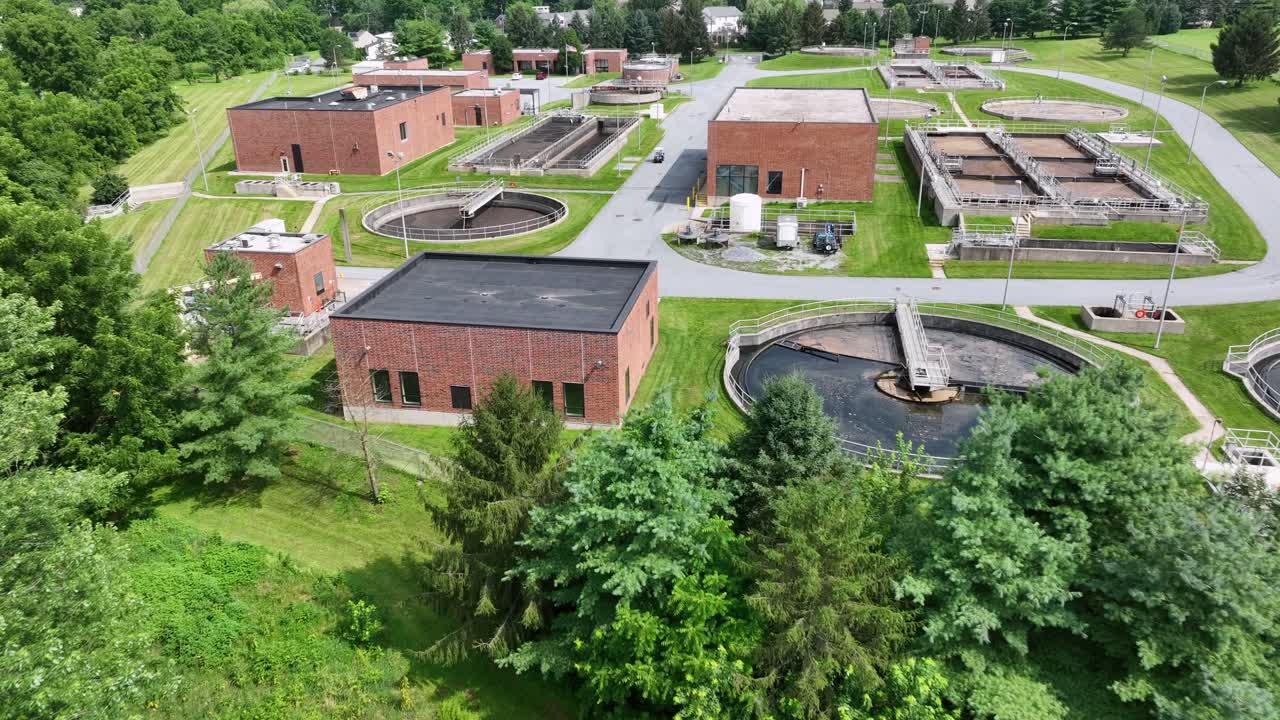 Aerial approaching shot of sewage treatment plant with red Brick buildings. Sunny summer Day in America. Water purification plant with sedimentation tanks in USA