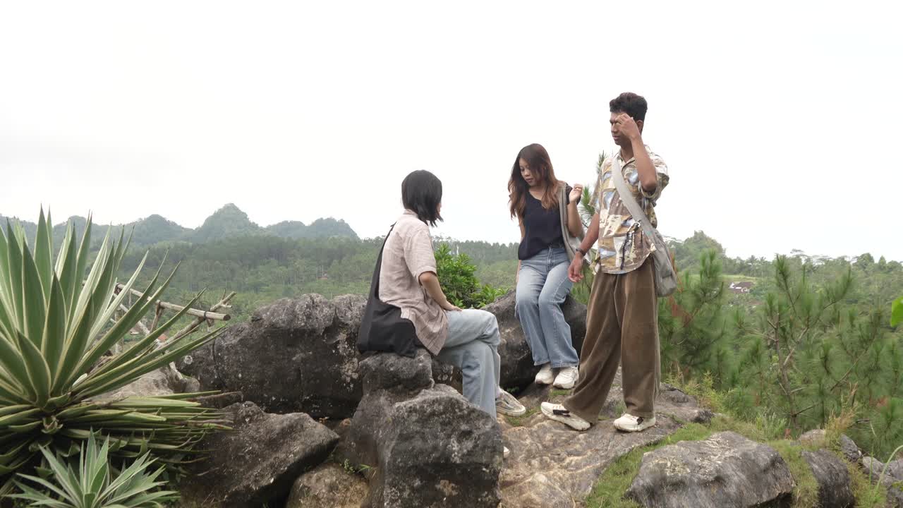 Young Asian Indonesian Friends Chatting and Laughing on Rocky Hilltop in Nature