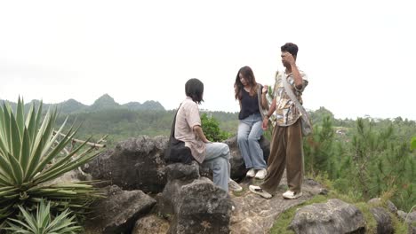 young asian indonesian friends chatting and laughing on rocky hilltop in nature