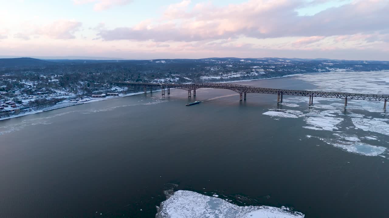 Geniş bir köprünün altında, suda yüzen büyük buz parçalarının görülebildiği Hudson Nehri'nin kış aylarındaki nefes kesen kuşbakışı manzarası. Karla kaplı tepelerle çevrili manzara huzurlu.