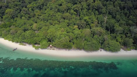 Aerial-shot-of-sandy-beach-with-beautiful-waters-and-natural-forest-in-Thailand---camera-tracking-backwards-pedestal-up
