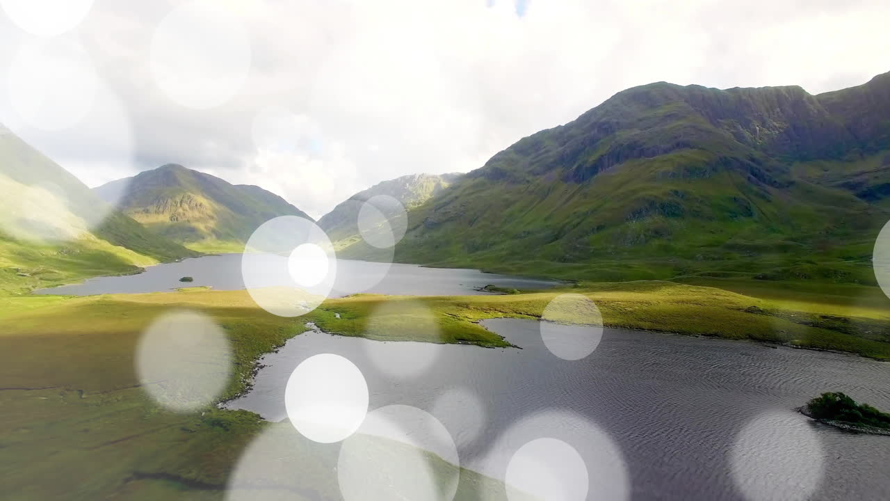 Animation of abstract circular light patterns over scenic mountain landscape with lake