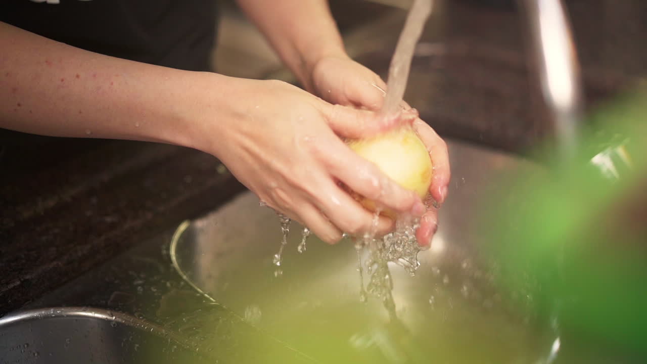 Manos femeninas lavando una cebolla blanca en el fregadero de la cocina en cámara lenta