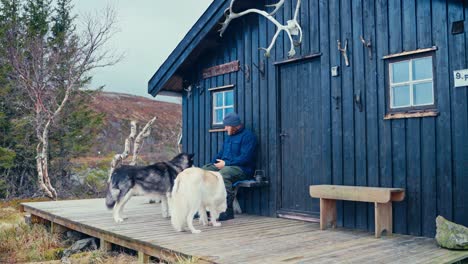 hiker and pet dogs resting outside a cabin in åfjord, norway - wide shot