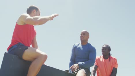 three diverse fit men high fiving in the sun after climbing fence at obstacle course