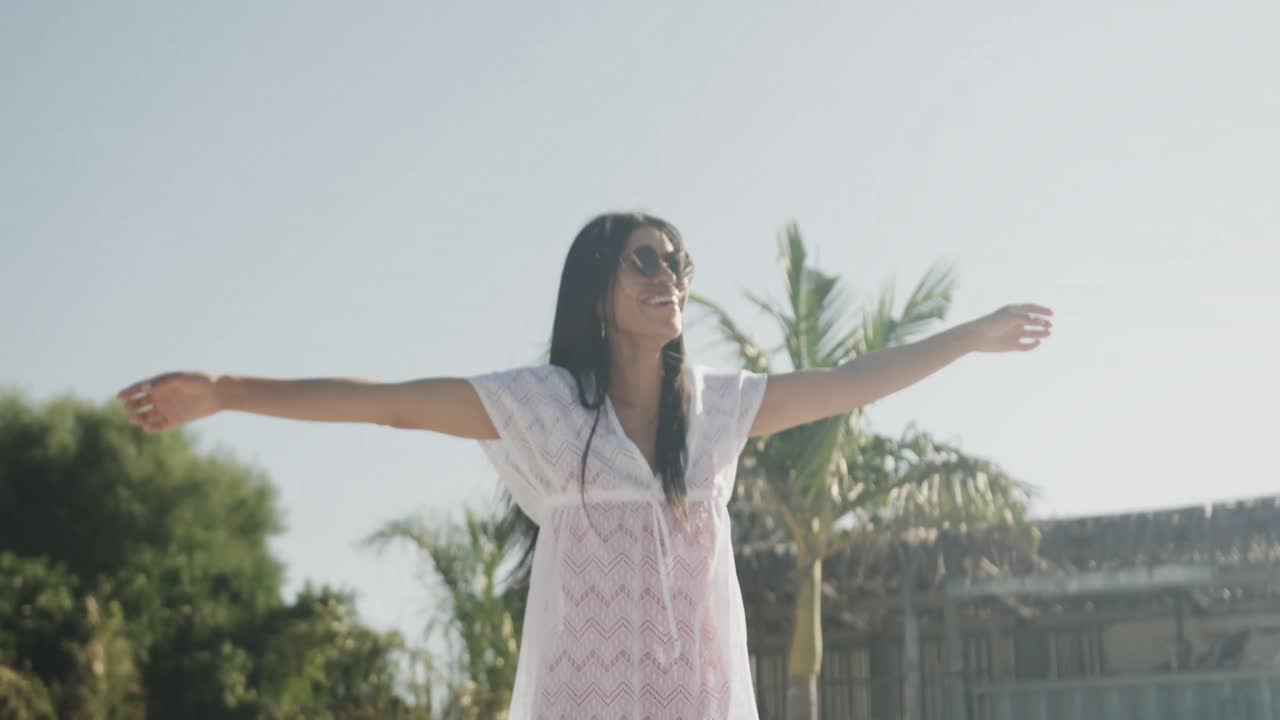 선글라스를 입은 행복한 히스패닉 여성이  ⁇ 빛 해변에서 춤을 추고, 미소 짓고, 슬로우 모션