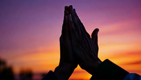 silhouetted hands of a couple join in prayer against a stunning sunset, creating a scene of love and spirituality