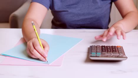 woman is using a calculator to calculate her monthly expenses and write down her monthly accounting records at home