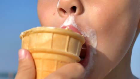 little hungry boy eating ice cream on the beach of the sea. the baby's face is smeared with ice cream.