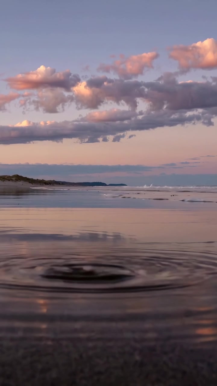 Vertical video: Mirroring tidal pool with tide, forming ripple, calming on beach under pink clouds