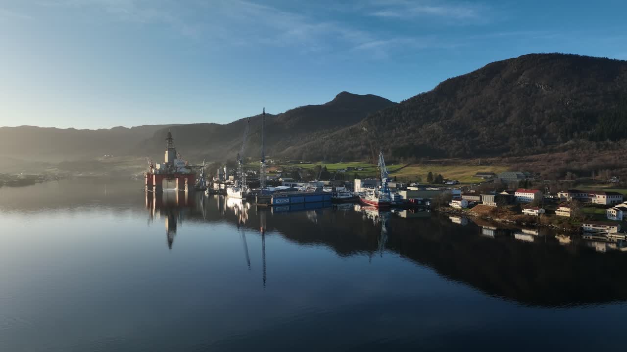 Evening aerial over Westcon Shipyard in Olensvag, Norway. Drilling rig and ships moored, glossy sea surface reflecting soft light