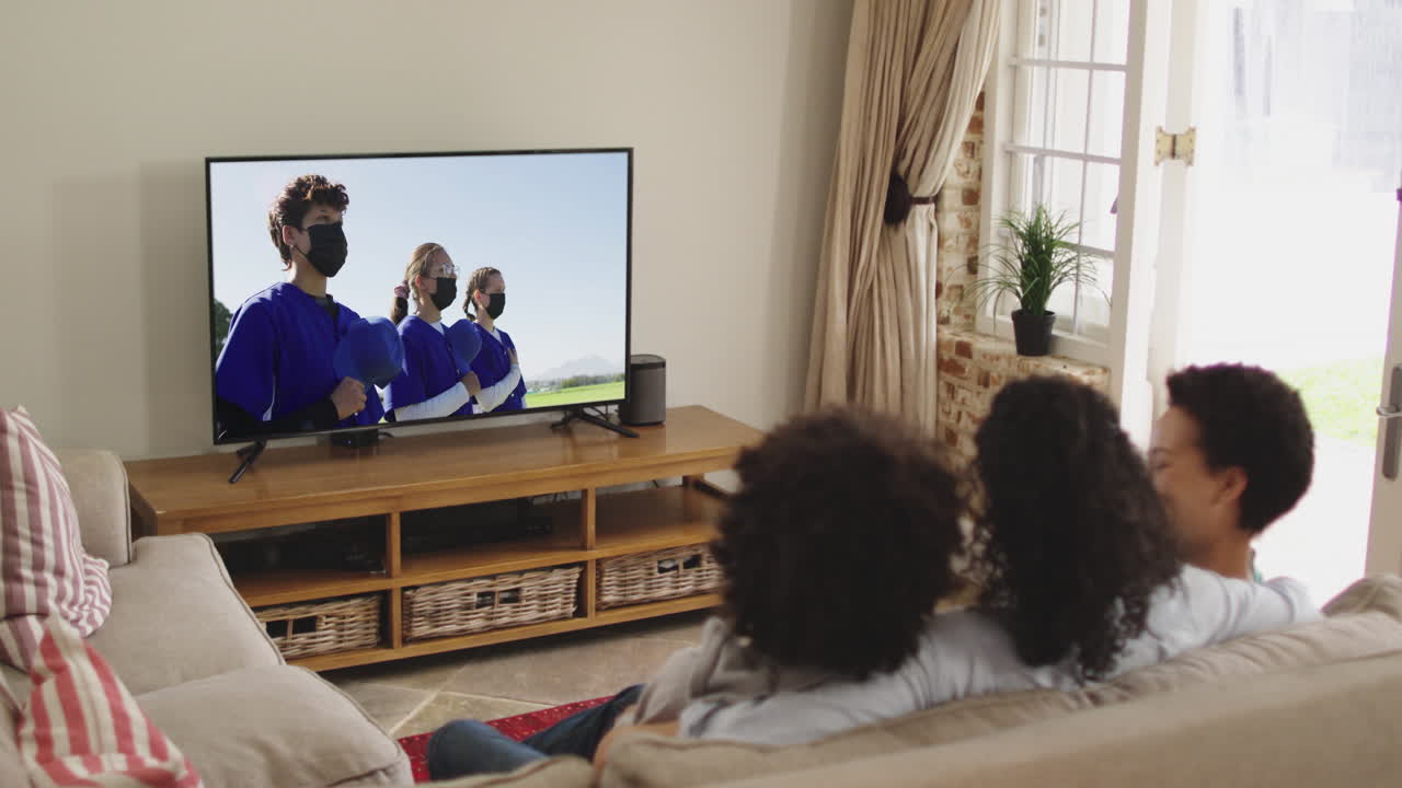 Famiglia felice seduta a casa insieme che guarda una partita di baseball in TV durante il COVID-19