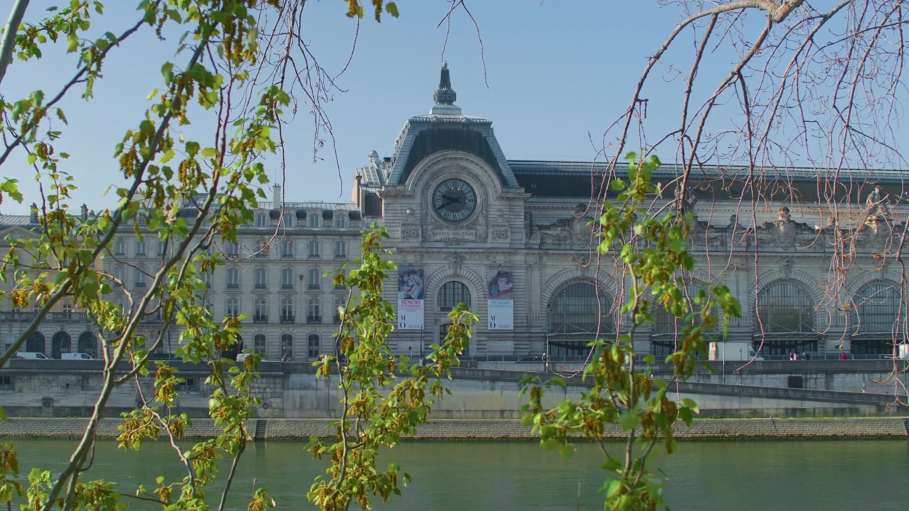 Ancien palais parisien vu depuis la rive, avec la circulation routière en contrebas, en plan large à main levée. Bâtiment historique français encadré par des feuilles d'arbres vertes au premier plan
