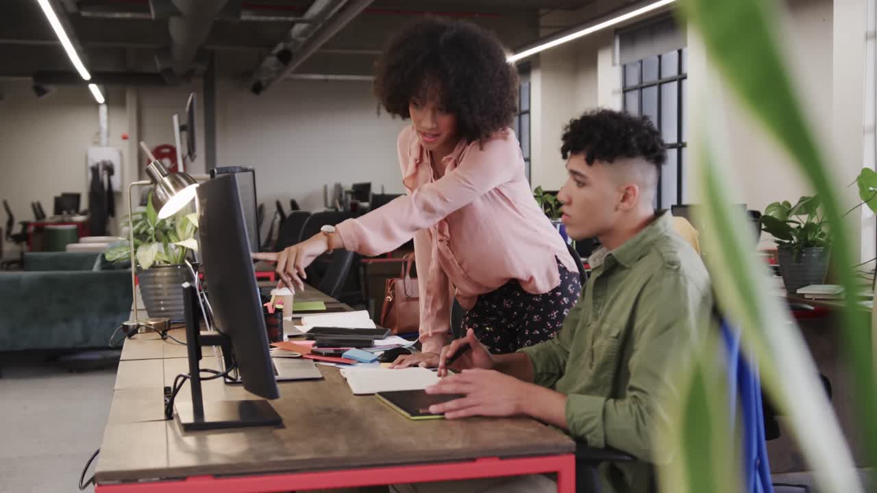 Two happy diverse creative designers in discussion at computer in casual office, slow motion