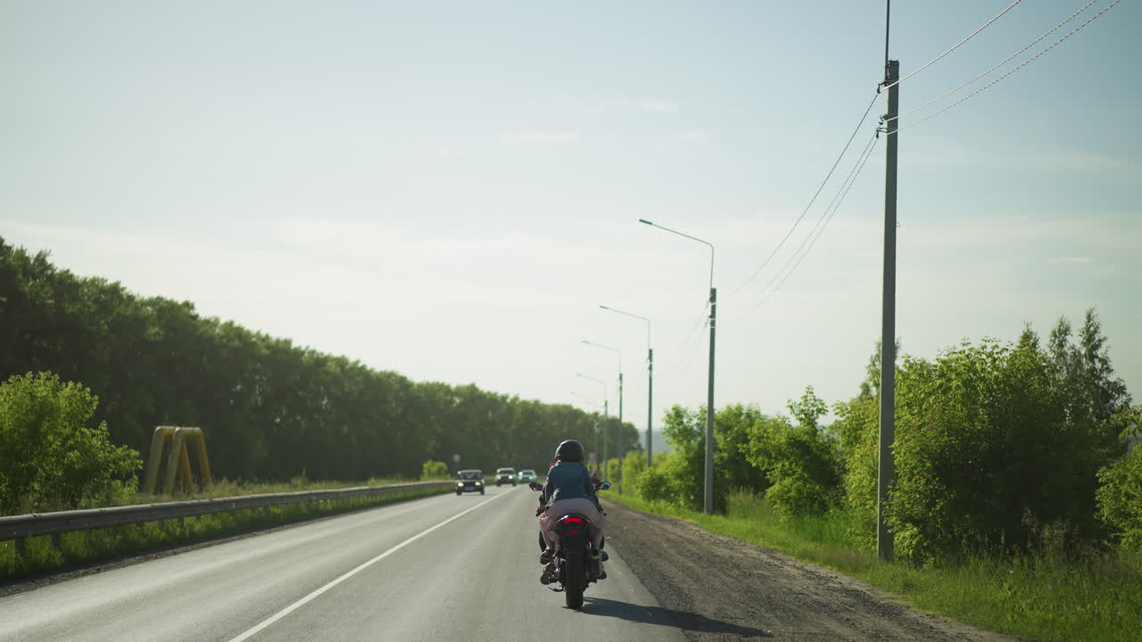 반대 방향에서 다가오는 자동차와 함께 느린 속도로 전력 자전거를 타고 있는 두 자매의 뒷면, 도로 표지판과 전기 기둥이 도로를 따라 보인다