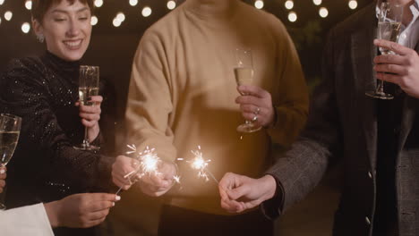 gruppe von vier multiethnischen freunden mit champagnergläsern, die sich auf der silvesterparty mit wunderkerzen amüsieren