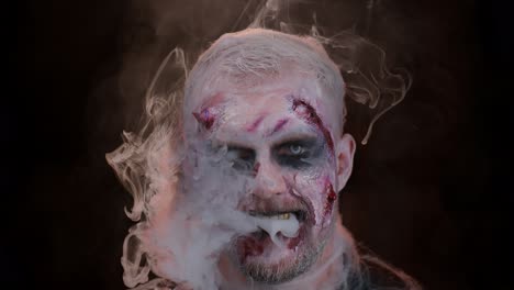 Sinister-man-horrible-scary-Halloween-zombie-looking-ominous-at-camera-blows-smoke-from-nose,-mouth