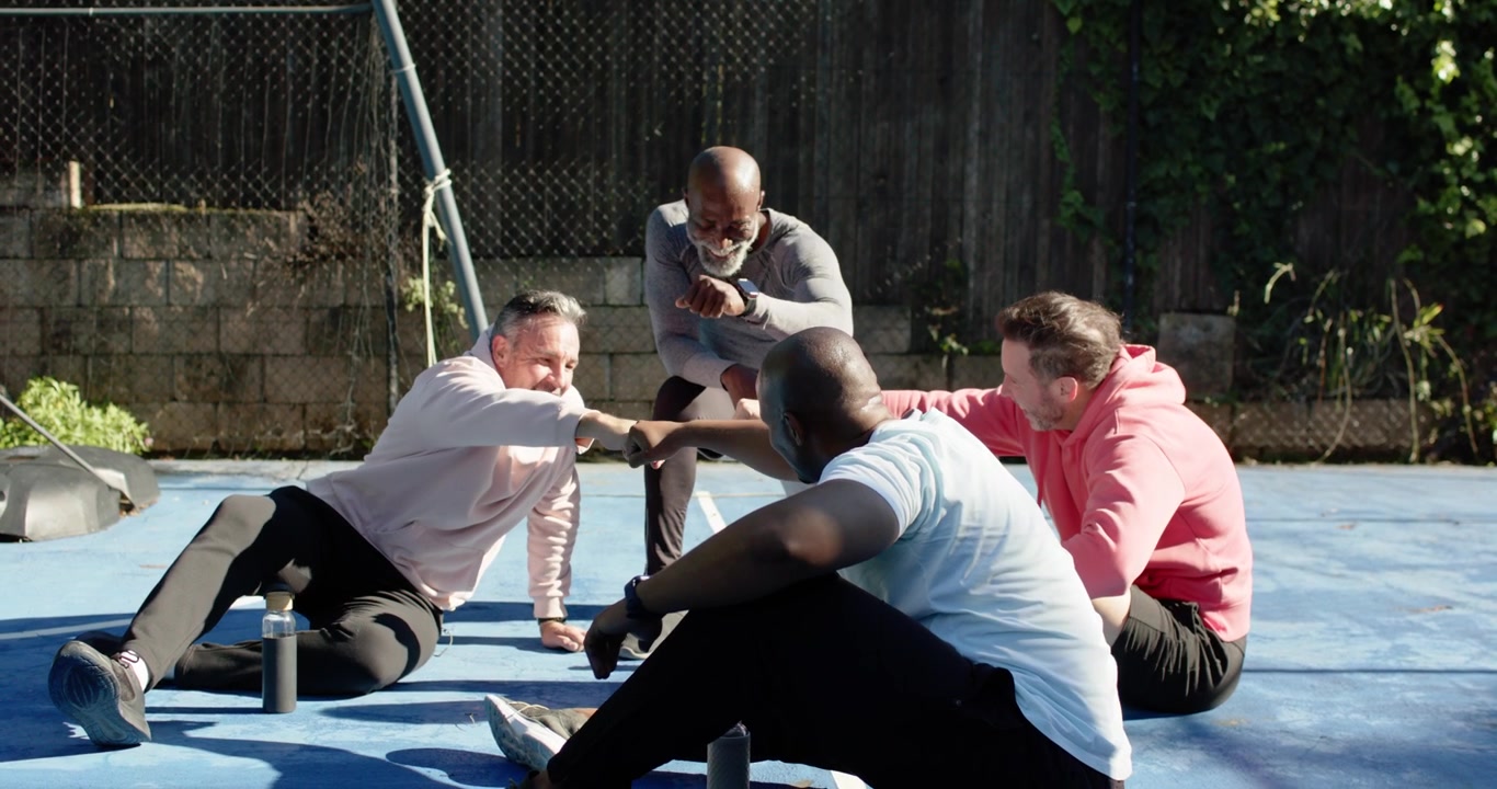 Diverse male friends fist bumping on blue court, kneeling African American man encouraging group