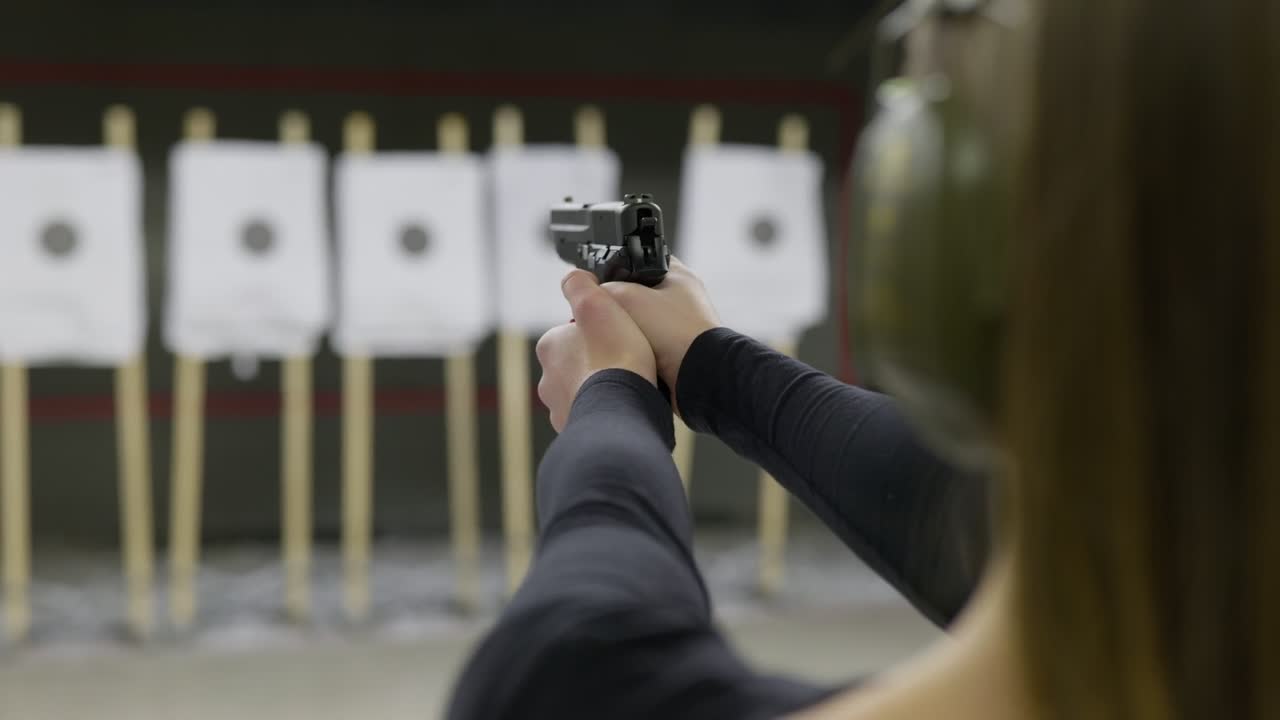 Woman Holding a Pistol Gun Practicing Shooting at Range from Behind